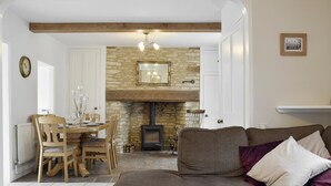 A cozy living room with a stone fireplace, wooden furniture, and a dining area. - 3 bedroom accommodation in Bampton, near Witney (Bampton, near Witney)