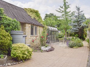 A stone house with a corrugated metal roof, a conservatory, and a garden with various plants and a pathway. - 3 bedroom accommodation in Bampton, near Witney (Bampton, near Witney)