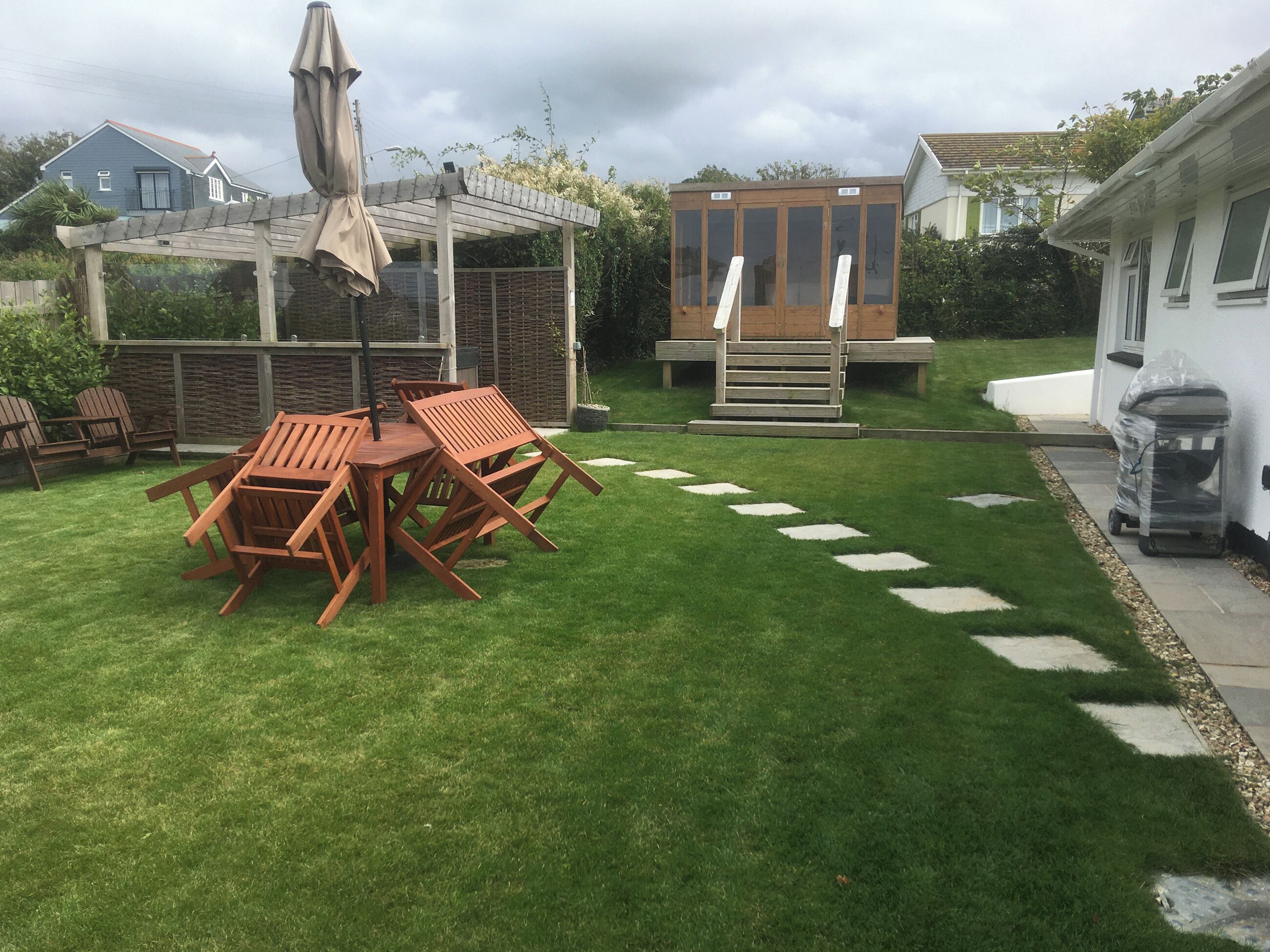 A backyard with a wooden table and chairs, a covered patio, and a small wooden structure.