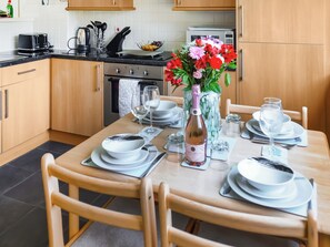 A kitchen with wooden cabinets, a stove, and a dining table set with plates, glasses, and a vase of flowers.