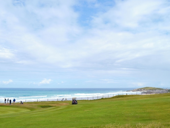 A golf course with a view of the ocean and a hilly landscape in the distance.