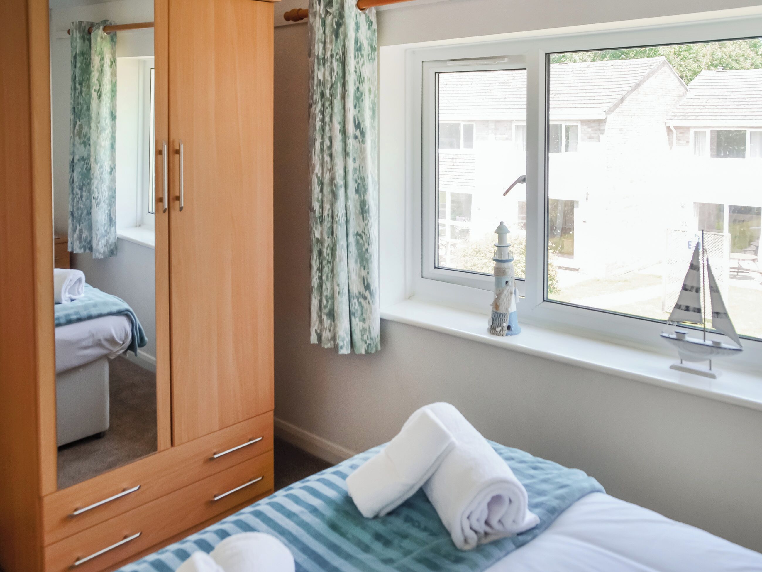 A bedroom with a bed, a wardrobe, a window with a view of houses, and a small decorative item on the windowsill.