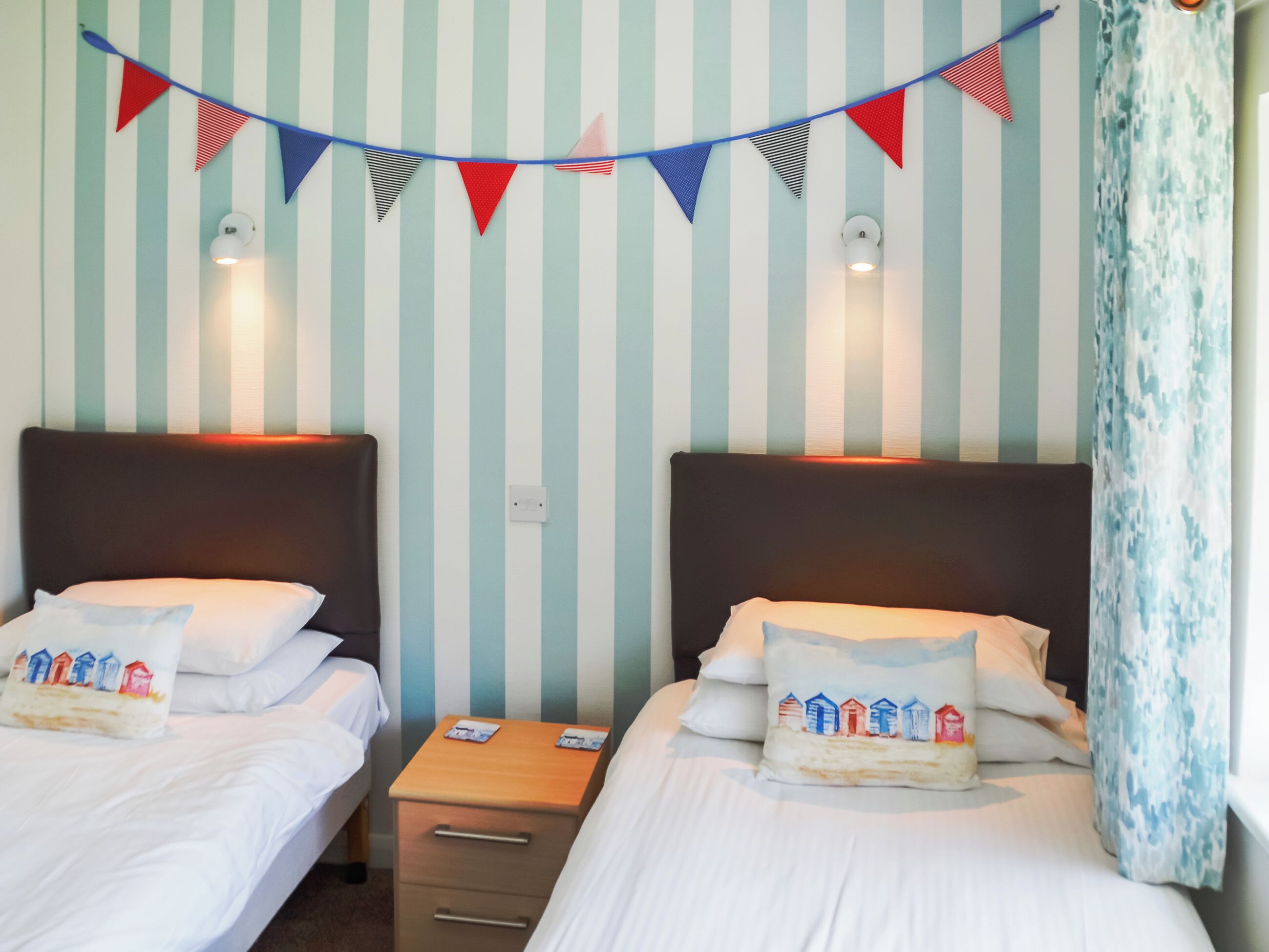 A hotel room with two beds, striped wallpaper, and a string of bunting.