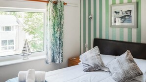 Une chambre à coucher avec un lit, des oreillers, une fenêtre donnant sur une maison, un rideau et un tableau encadré accroché au mur.