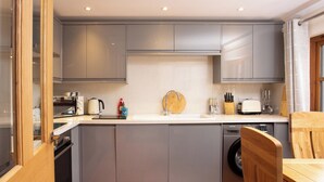 Una cocina compacta con armarios grises, lavadora integrada y una mesa de comedor de madera.