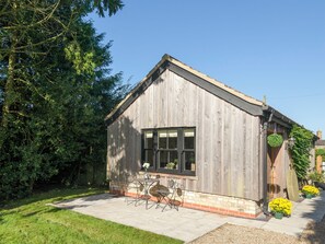 Een klein houten gebouw met een raam, een deur en een klein terras met een tafel en stoelen.