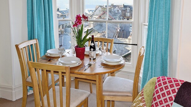 A dining area with a bay window overlooking a cityscape. - 2 bedroom accommodation in Bowness-on-Windermere (Bowness-on-Windermere)