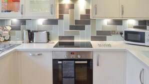 A modern kitchen with white cabinets, a built-in oven, a microwave, and a kettle. - 2 bedroom accommodation in Bowness-on-Windermere (Bowness-on-Windermere)