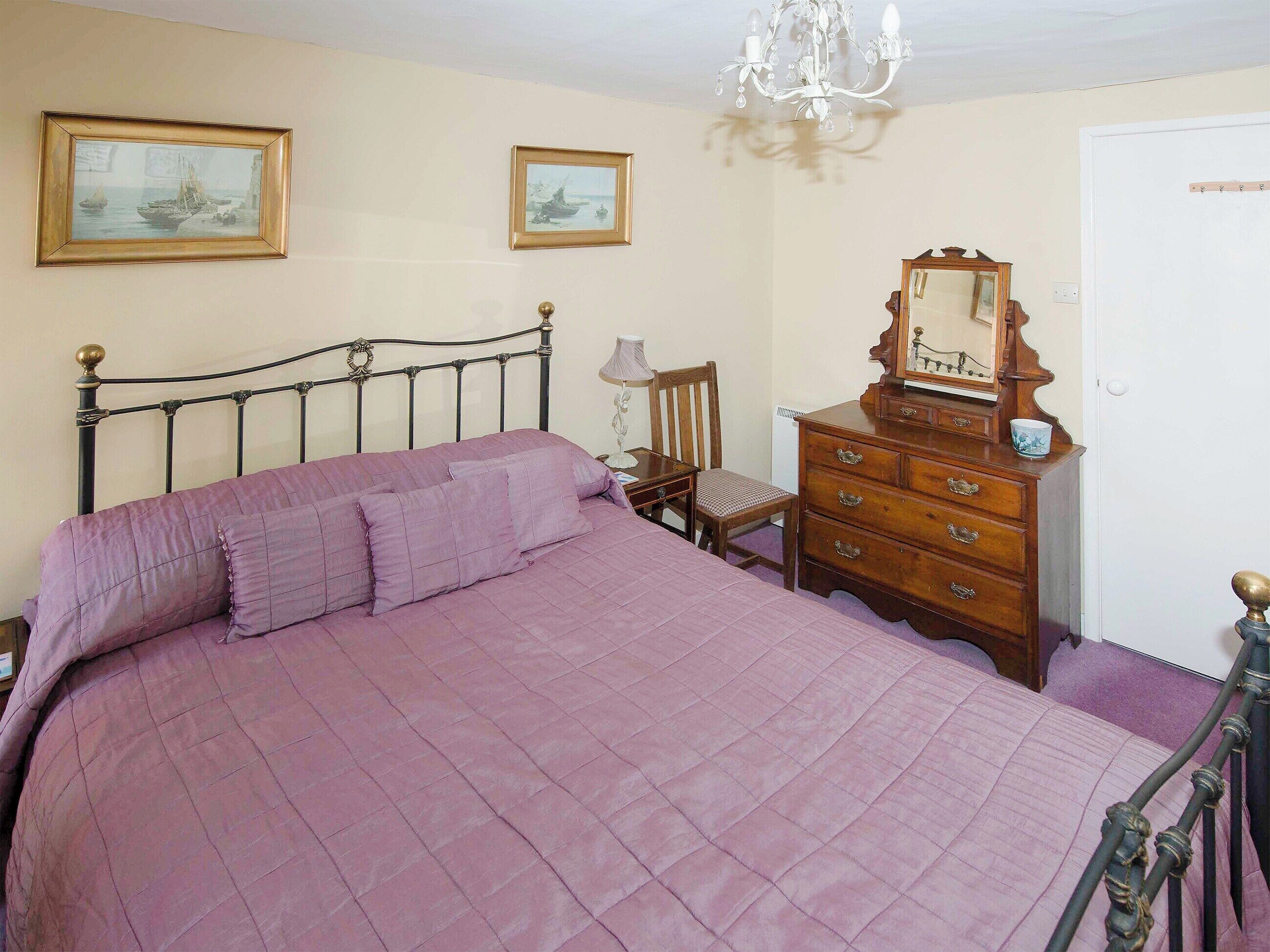 Une chambre à coucher avec un lit, une commode, une chaise et deux tableaux encadrés accrochés au mur.