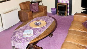 A living room with a fireplace, leather sofas, a coffee table, and a television. - The Plover - UKC2845 (Blakeney, near Holt)