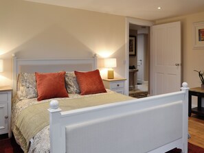 Un dormitorio con cama, mesitas de noche, lámpara, puerta y una pequeña mesa con una planta.
