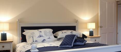 A bedroom with a bed, two bedside tables, a nightstand, a door, and a lamp.