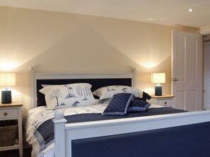 Un dormitorio con una cama, dos mesitas de noche, una lámpara y una puerta.