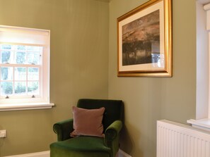Una habitación con un sillón verde, una ventana con persianas, un radiador y un cuadro en la pared.