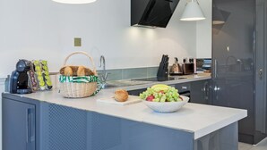 Une cuisine moderne avec un îlot central, une machine à café, un panier et un saladier rempli de fruits.
