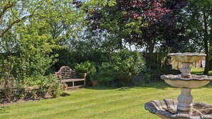 Un jardin agrémenté d’une fontaine en pierre, d’un banc en bois et d’un mur de pierres.