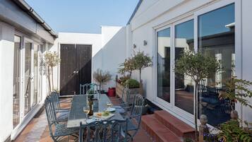 Eine Terrasse mit Esstisch und Stühlen, umgeben von einem kleinen Garten mit Topfpflanzen.