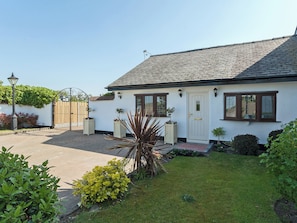 A white house with a tiled roof, a front door, and a small garden with plants and a lamp post.
