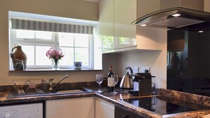 A modern kitchen with a built-in washing machine, a stainless steel kettle, and a wine bottle on the counter. - Cowbeech Farm Cottage (Cowbeech, near Hailsham)