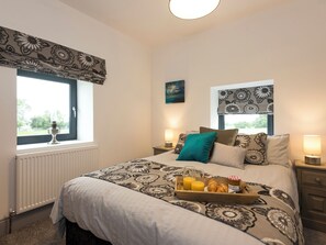 A bedroom with a large bed, a window with a view, a bedside table with a lamp, and a tray with breakfast items. - Moorgate Cottage - UKC3380 (Kelbrook, near Barnoldswick)