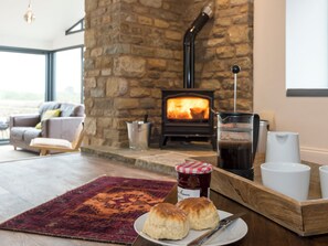 A cozy room with a stone fireplace, a coffee table with biscuits and jam, and a view of the outdoors. - Moorgate Cottage - UKC3380 (Kelbrook, near Barnoldswick)