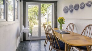 Et spiseområde med et træbord og stole, en vase med gule blomster og udsigt til det frie gennem en glasdør.