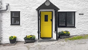 En hvid bygning med gul dør, sorte skodder og to blomsterkrukker foran.