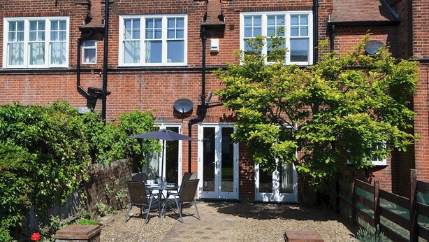 A brick house with a patio area, a small table with chairs, and a tree. - 2 bedroom accommodation in Sheringham (Sheringham)