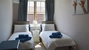 A hotel room with two beds, a window with curtains, a lamp, and a giraffe artwork on the wall. - 2 bedroom accommodation in Sheringham (Sheringham)