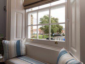 Ein Zimmer mit einem großen Fenster, einer Bank mit gestreiften Kissen und Blick auf eine Straße und Gebäude.