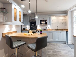 A modern kitchen with a wooden island, two bar stools, a microwave, and a wine bottle.