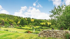 Un paisaje exuberante con colinas ondulantes, un muro de piedra y una estatua en primer plano.