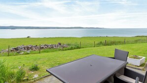 A patio with a table and chairs overlooking a body of water and grassy landscape. - 3 bedroom accommodation in Gairloch (Gairloch)