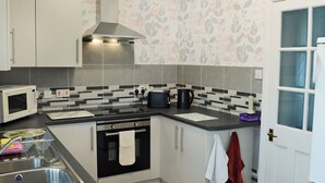 A compact kitchen with a microwave, toaster, kettle, and oven. There is a sink with a dish rack, and a window with frosted glass. - 1 bedroom accommodation in Bunbury (Bunbury)