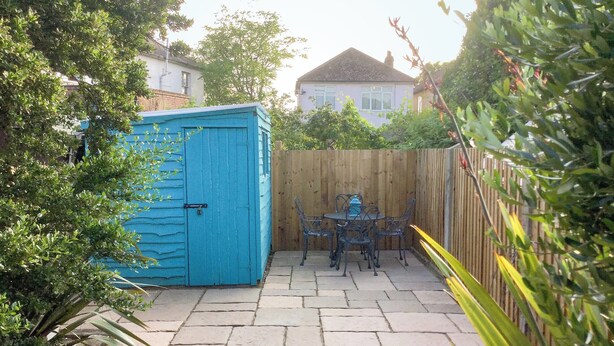 A patio with a blue shed, a wooden fence, and a table with chairs.