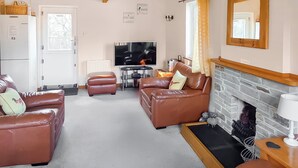 A living room with two brown leather sofas, a television, a fireplace, and a dining area with a table and chairs. - 3 bedroom accommodation in St Mellion, near Saltash (St Mellion, near Saltash)