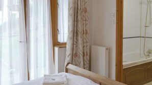 A bedroom with a bed, a window with sheer curtains, a radiator, and a shower area. - 3 bedroom accommodation in St Mellion, near Saltash (St Mellion, near Saltash)