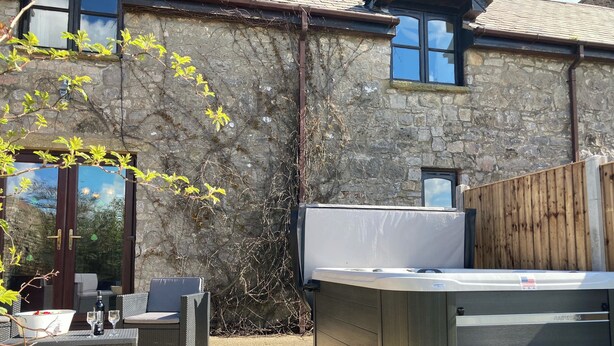 A patio area with a hot tub, outdoor seating, and a stone wall. - 2 bedroom accommodation in Trelawnyd, near Prestatyn (Trelawnyd, near Prestatyn)