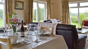 A dining area with a table set for four, a sofa with a checkered throw, and a view of the outdoors through large windows. - 2 bedroom accommodation in Acharacle (Acharacle)