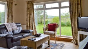 A living room with a leather sofa, a wooden coffee table, a wicker chair, and a television on a stand. - 2 bedroom accommodation in Acharacle (Acharacle)