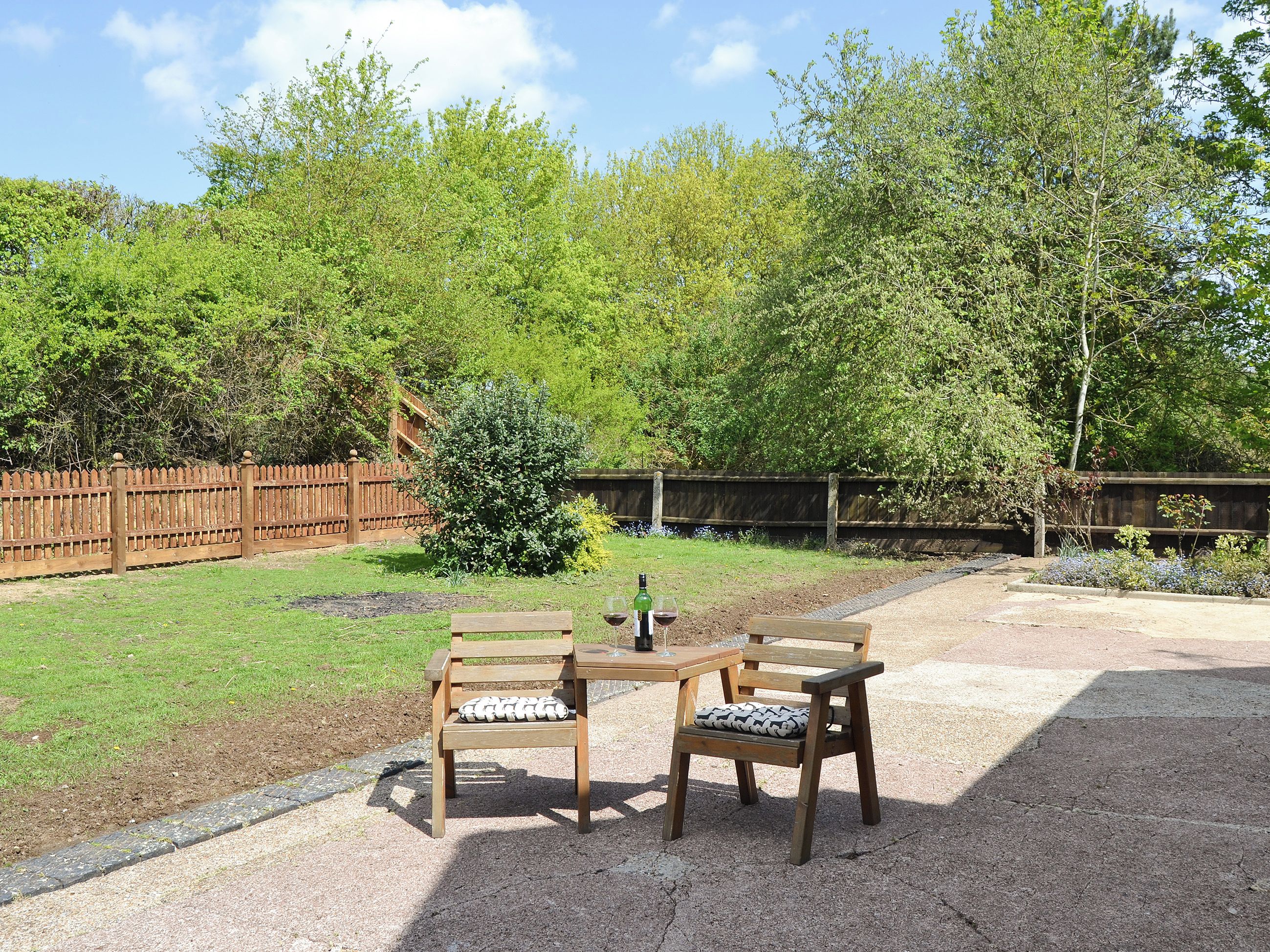 An outdoor seating area with two wooden tables and chairs, a small bush, and a wooden fence.