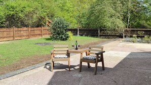 Een terras buiten met twee houten tafels en stoelen, een kleine struik en een houten omheining.
