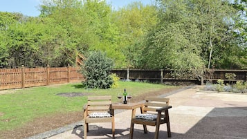 An outdoor seating area with two wooden tables and chairs, a small bush, and a wooden fence.
