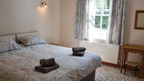 Een slaapkamer met een bed, bloemenbedrijf, een nachtkastje, een raam met gordijnen en een radiator.