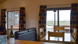 A dining area with a wooden table, chairs, a sofa, and a bottle of wine. - 2 bedroom accommodation in Burgh le Marsh, near Skegness (Burgh le Marsh, near Skegness)