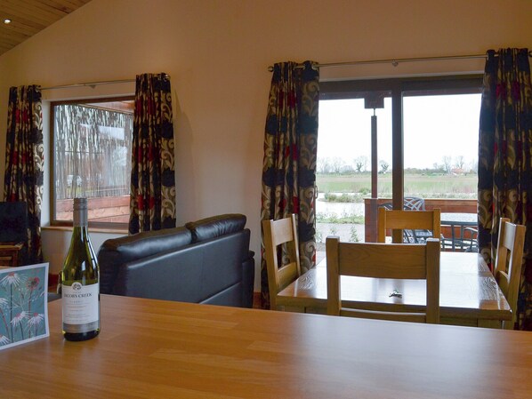 A dining area with a wooden table, chairs, a sofa, and a bottle of wine. - 2 bedroom accommodation in Burgh le Marsh, near Skegness (Burgh le Marsh, near Skegness)