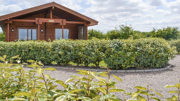 A wooden cabin with a covered porch, surrounded by well-maintained hedges and a gravel path. - 2 bedroom accommodation in Burgh le Marsh, near Skegness (Burgh le Marsh, near Skegness)