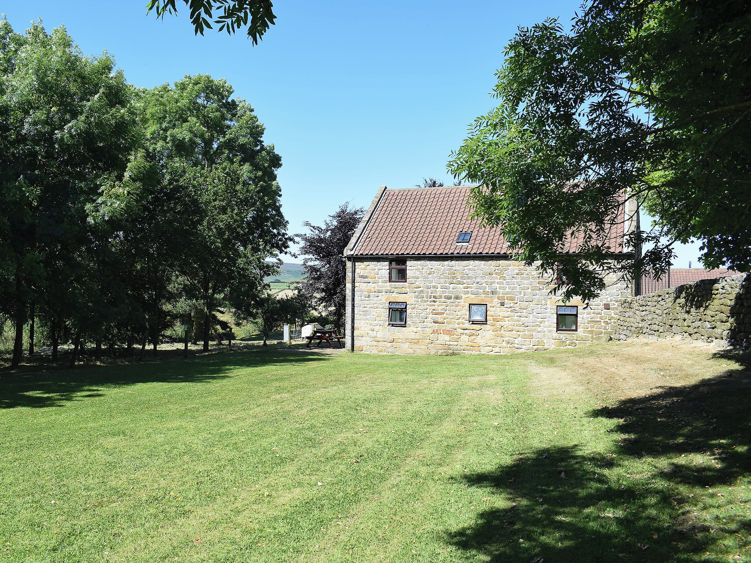 A stone building with a tiled roof, surrounded by a grassy area and trees.