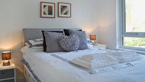 Un lit bien fait, avec du linge de lit blanc et une serviette blanche pliée, deux lampes de chevet et deux tableaux encadrés accrochés au mur.
