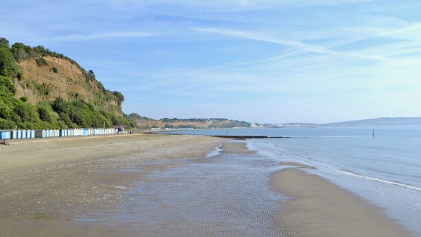 Une plage avec un rivage sablonneux, une falaise rocheuse et un ciel d égagé.